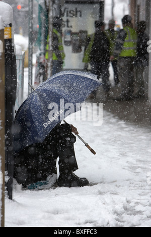 Straße Bettler sitzen unter Deloitte Dach im Schnee an einem kalten verschneiten Winter Tag Belfast Nordirland Stockfoto