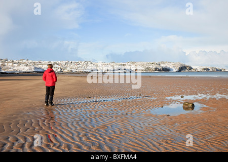 Frau trägt eine rote Jacke Wandern auf nassem Sand auf einem leeren Sandstrand bei Ebbe mit Schnee im Winter 2010. Benllech, von der Insel Anglesey im Norden von Wales UK Stockfoto