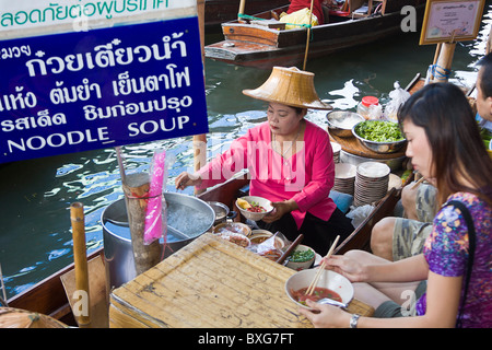 Frau Anbieter in Khlong Boot verkauft Suppe an junge Frau am Damnoen Sakuak schwimmende Markt außerhalb Bangkok, Thailand Stockfoto