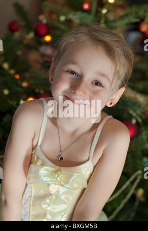 Kleines Mädchen in einem Prinzessin Belle Kostüm mit einem Weihnachtsbaum im Hintergrund Stockfoto