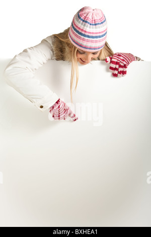 Frau in bunte Mütze und Handschuhe lugt hinter Whiteboard isoliert auf weiss Stockfoto