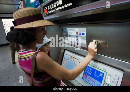 Frau und ihr Sohn eine Einzelfahrt-Ticket von einem Ticket ausstellen Maschine in der u-Bahn, Hong Kong Insel, China zu kaufen. Stockfoto