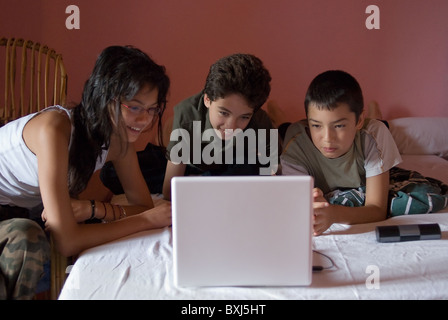 Drei Kinder liegend auf einem Bett mit einem Laptop, Frankreich. Stockfoto