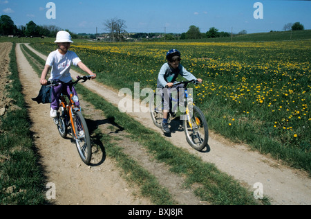 Jungen und Mädchen, Radfahren auf einer unbefestigten Straße durch die Landschaft zusammen. Stockfoto