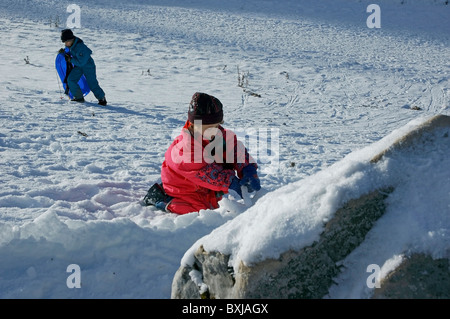 Kleines Mädchen im Schnee alleine zu spielen, während ihr Bruder Rodeln geht. Stockfoto