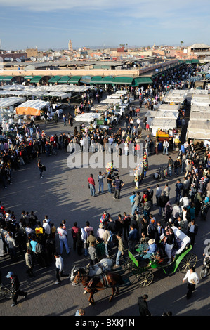 Blick auf Djemaa el-Fna Treffpunkt mit Leistung mit Menschenmenge versammelt Turm der Koutoubia-Moschee Stockfoto