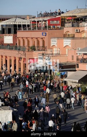 Menschenmassen herumlaufen beschäftigt Djemaa el-Fna Treffpunkt mit Cafés & Restaurants in Marrakesch Stockfoto