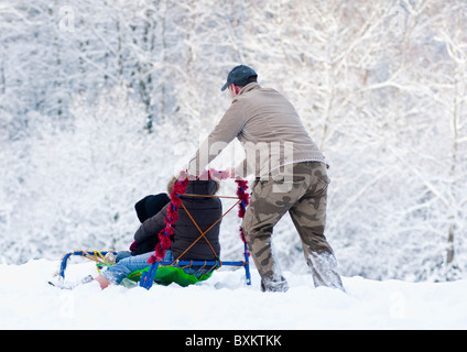 Vater schiebt sein Kind Schlitten hinunter den Hügel in Worcestershire, England, im Winter des Jahres 2010. Stockfoto