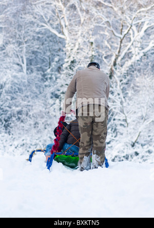 Vater schiebt sein Kind Schlitten hinunter den Hügel in Worcestershire, England, im Winter des Jahres 2010. Stockfoto