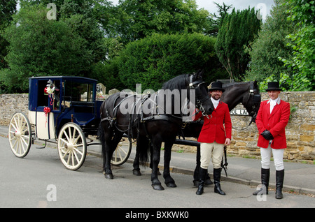 Eine Pferdekutsche Hochzeitskutsche mit zwei livrierte Treiber in das Dorf Harpole, Northamptonshire, UK Stockfoto