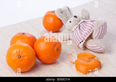 Happy toy wenig Damhirschkuh, die Kaninchen in der Nähe von dem Haufen von Reife frische Mandarinen aufliegt Stockfoto