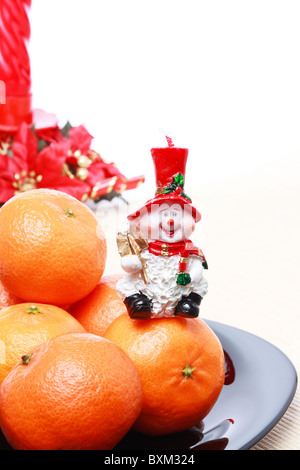 Haufen von Reife frische Orangen Mandarinen auf schwarzem Teller, Schneemann mit goldenen Spaten und rote Kerze mit Weihnachtsdekoration Stockfoto