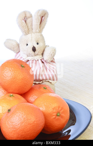 Spielzeug, kleine Doe Kaninchen und Haufen von Reife frische Orangen Mandarinen auf schwarzen Druckplatte Stockfoto