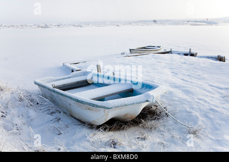 Zwei Ruderboote am Rand ein Loch gefesselt neben einem kleinen Pier. Boote bedeckt mit Schnee und Frost Stockfoto