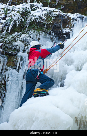 Männliche Bergsteiger wird während einer Eisklettern auf einem gefrorenen Wasserfall (Lynn fällt) außerhalb Dalry in North Ayrshire, Schottland gesichert. Stockfoto