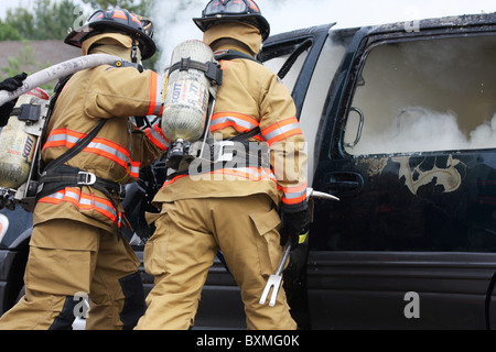 Feuerwehrleute auf einem Neuanschluß Löschangriff ein Auto Stockfoto