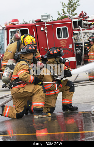 Feuerwehrleute auf einem Neuanschluß Löschangriff mit einer Reflexion über den nassen Boden Stockfoto