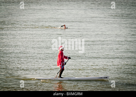 Eine gehärtete Schwimmer und ein Weihnachtsmann auf einem Kanu nehmen in eine Unterroutine Null Meer am Weihnachtstag auf Brighton Beach für das jährliche Xmas-schwimmen. Stockfoto
