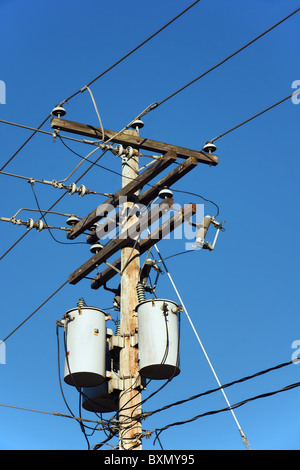 Transformatoren von einem elektrischen Post mit Stromleitung gegen strahlend blauen Himmel. Stockfoto