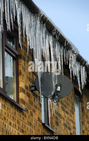 Es gibt viele große Eiszapfen hängen von einem Dach und Satellitenschüssel. Oxfordshire, Vereinigtes Königreich, 2010. Stockfoto