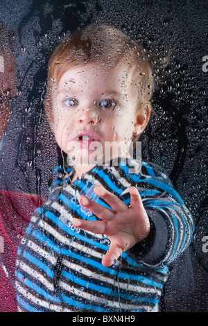 Kleiner Junge spielt mit Kondenswasser am Fenster Stockfoto