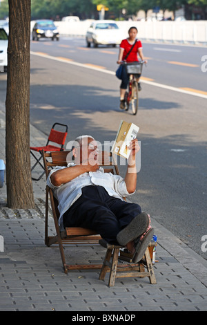 Mann liest Buch auf Bürgersteig, Peking, China Stockfoto