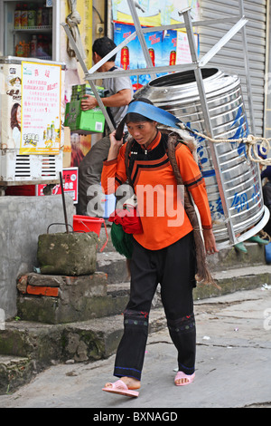 Yi ethnische Minderheit Frau trägt Edelstahl Metallbehälter / Wassertank auf der Rückseite in Yuanyang, Provinz Yunnan, China Stockfoto