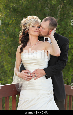 Brautpaar stehend auf Brücke umarmen Bräutigam küssen Braut Stockfoto