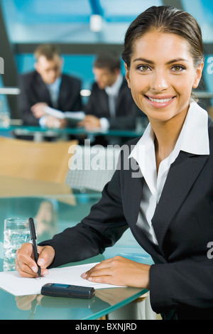 Portrait der schönen Frau schreiben auf dem Hintergrund von zwei Geschäftsleuten im Konferenzraum Stockfoto