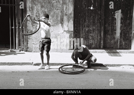 Zwei Jungen, die auf den Straßen von Havanna, Kuba, mit Fahrradrädern spielen. Stockfoto