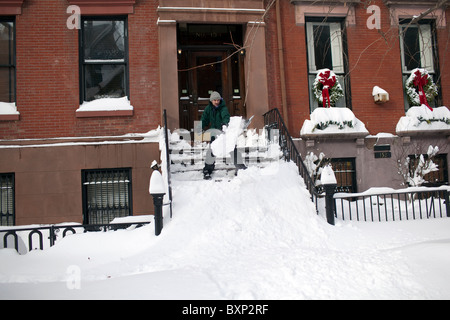 Ein Mann schaufelt eine Veranda nach einem massiven Schneesturm die Straßen in Brooklyn, New York geschlossen. Stockfoto