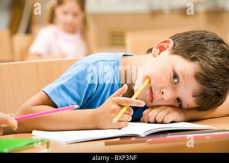 Nahaufnahme der müde Schüler mit gelben Buntstift er seinen Kopf auf den Arm und Blick in die Kamera Stockfoto