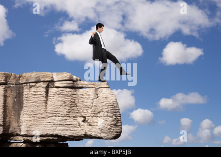 Geschäftsmann, eine Gefahr und Schritt aus einem Felsen fallen Stockfoto