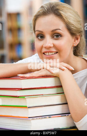 Porträt der hübsche Studentin, indem ihr Kinn auf der Seite über Stapel Bücher Stockfoto