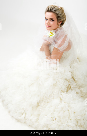 Foto von elegant Braut in modischen Ehe mit Blume in der hand sitzen und Blick in die Kamera Stockfoto