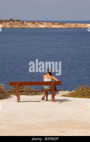 Weibliche Touristen sitzen auf einer Bank mit Blick auf Meer, Governors Beach, Cape Delosse, Zypern Stockfoto