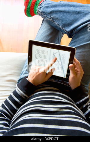 Mann Entspannung zu Hause mit einem Apple Mac iPad zum Lesen eines Buches von iBooks auf seinem Schoß. Stockfoto