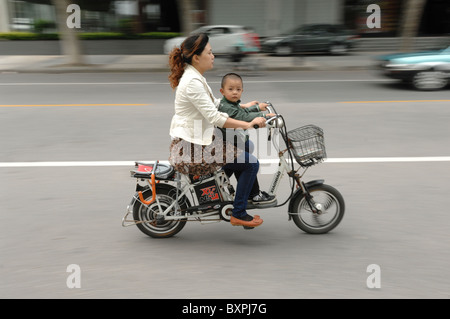 Eine Frau und junge Kind reiten ein Elektroroller entlang einer Straße in Yangzhou Jiangsu Provinz in China Stockfoto