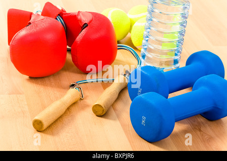 Foto von zwei blauen Hanteln, paar Tennisbälle, Flasche Wasser und Boxhandschuhe auf Holzuntergrund Stockfoto