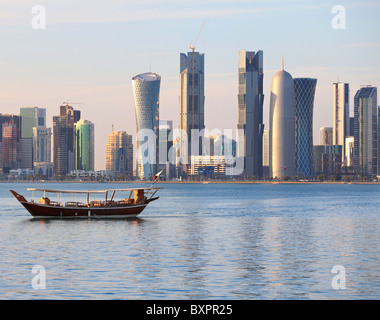 Eine Dhau kehrt zurück, um in Doha, Katar, Hafen bei Sonnenuntergang, mit modernen Skyline der Stadt im Hintergrund. Stockfoto