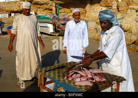 Fischhändler schneiden Fisch für zwei arabische Kunden an eine Open-Air-Marktstand, Sur, Sultanat von Oman Stockfoto