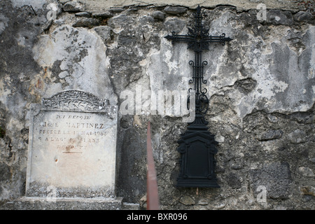 Ein Grabstein und ein Kreuz an einer zerbröckelnden Wand in einem französischen Friedhof. Stockfoto