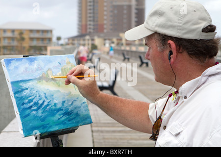 Künstler stehen auf einem Pier und anhören von Musik über Kopfhörer verwendet eine eckige Pinsel hinzufügen, eine Leinwand-Highlights montiert p Stockfoto