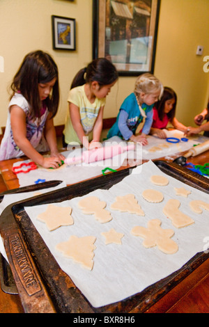 Zwei Filipino/weißen Schwestern und ihren weißen und japanischen Freunden ausrollen und schneiden Sie Zucker Cookies auf dem Küchentisch. Stockfoto