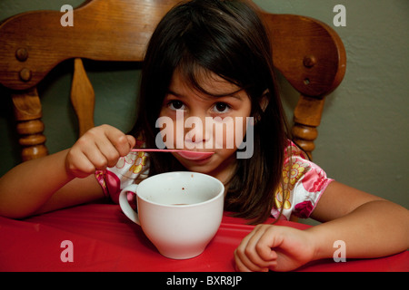 Filipino/weiß Mädchen trinken heißen Schokolade aus einer großen weißen Tasse am Küchentisch Stockfoto