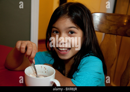 Filipino/weiß Mädchen trinken heißen Schokolade aus einer großen weißen Tasse am Küchentisch Stockfoto