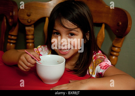 Filipino/weiß Mädchen trinken heißen Schokolade aus einer großen weißen Tasse am Küchentisch Stockfoto