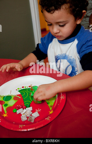 Three-Year-Old Mexican American Boy dekoriert ein Lebkuchen am Küchentisch Stockfoto