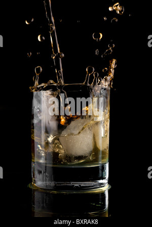 Glas Whisky auf einem schwarzen Hintergrund. Whisky-Spritzer in ein Glas. Whisky mit Eis. Stockfoto