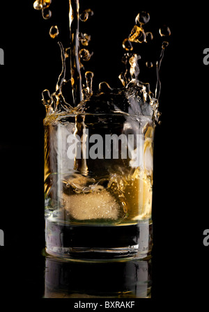 Glas Whisky auf einem schwarzen Hintergrund. Whisky-Spritzer in ein Glas. Whisky mit Eis. Stockfoto